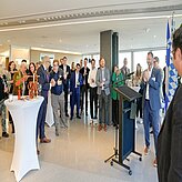 Delegation in einem hellen Innenraum bei einer Veranstaltung mit Rednerpult und Stehtischen. Entstanden im Rahmen der Delegationsreise in Kanada.