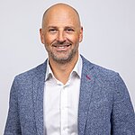 Oberkörperaufnahme eines Mannes mit weißem Hemd und blauem Sakko vor hellem Hintergrund