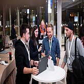 Eine Gruppe Menschen steht an einem Stehtisch und unterhält sich