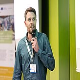 Ein Mann hält einen Vortrag, er steht vor einem grünen Hintergrund