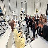 Führung: Robotik und Design im Deutschen Museum: Eine Gruppe von Menschen versam-melt sich vor einem humanoiden Roboter und einem Roboter, der auf einem Fahrradgestell sitzt.