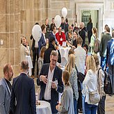 Menschen auf einer Konferenz in einem Gebäude, umgeben von bunten Luftballons, die eine festliche Atmosphäre schaffen