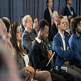 People sitting in front of the Thinknet 6G Summit stage, listening to the speaker and taking notes.