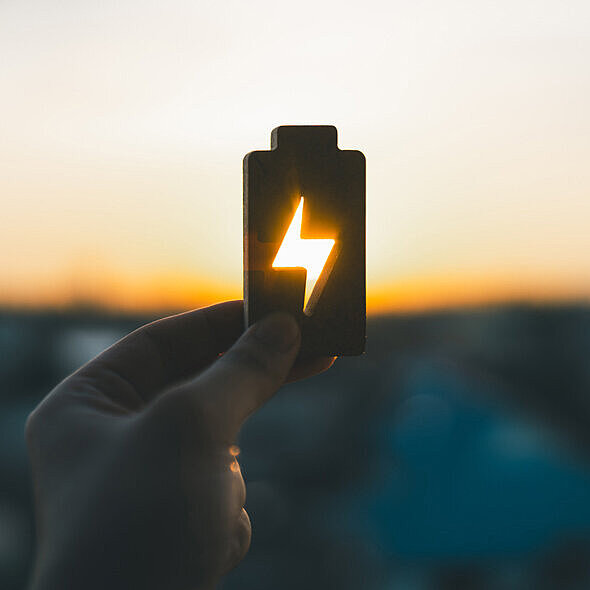Ein Symbol einer Batterie wird vor einem Sonnenuntergang hochgehalten