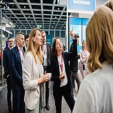 Gruppe von Menschen mit Namensschildern in einem modernen Innenraum, eine Frau zeigt mit dem Finger nach oben