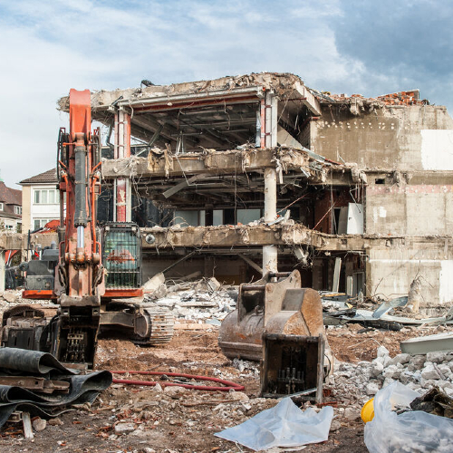 Ein Gebäude, dass abgerissen wird. Ein Bagger steht daneben.
