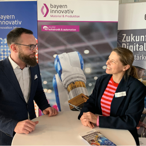 Eine Frau und ein Mann sprechen am Messestand von Bayern Innovativ