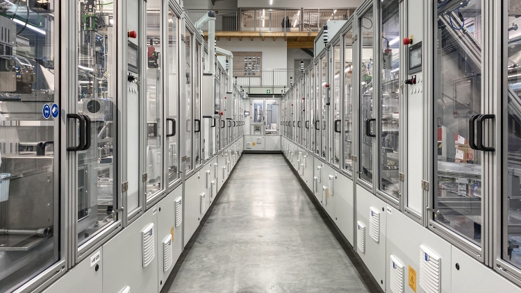 Beispielanlage der AKE technologies GmbH: Moderner Industrieflur in grauen, metallischen Tönen mit Glastüren auf beiden Seiten, die Einblicke in technische Geräte und Maschinen ermöglichen.